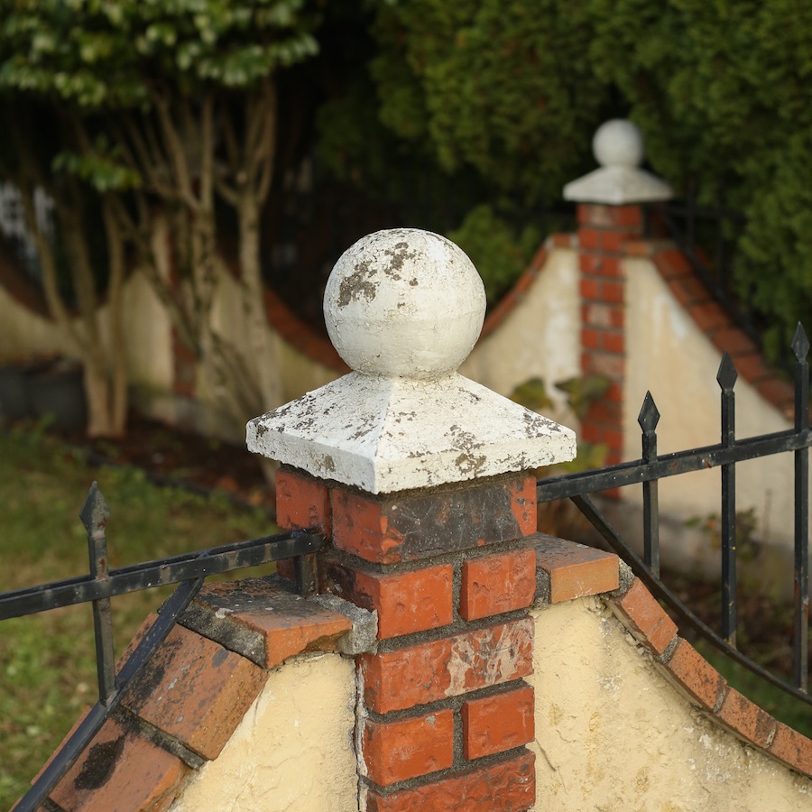 A little concrete figurine of a ball on a pedestal on the post of a brick fence.