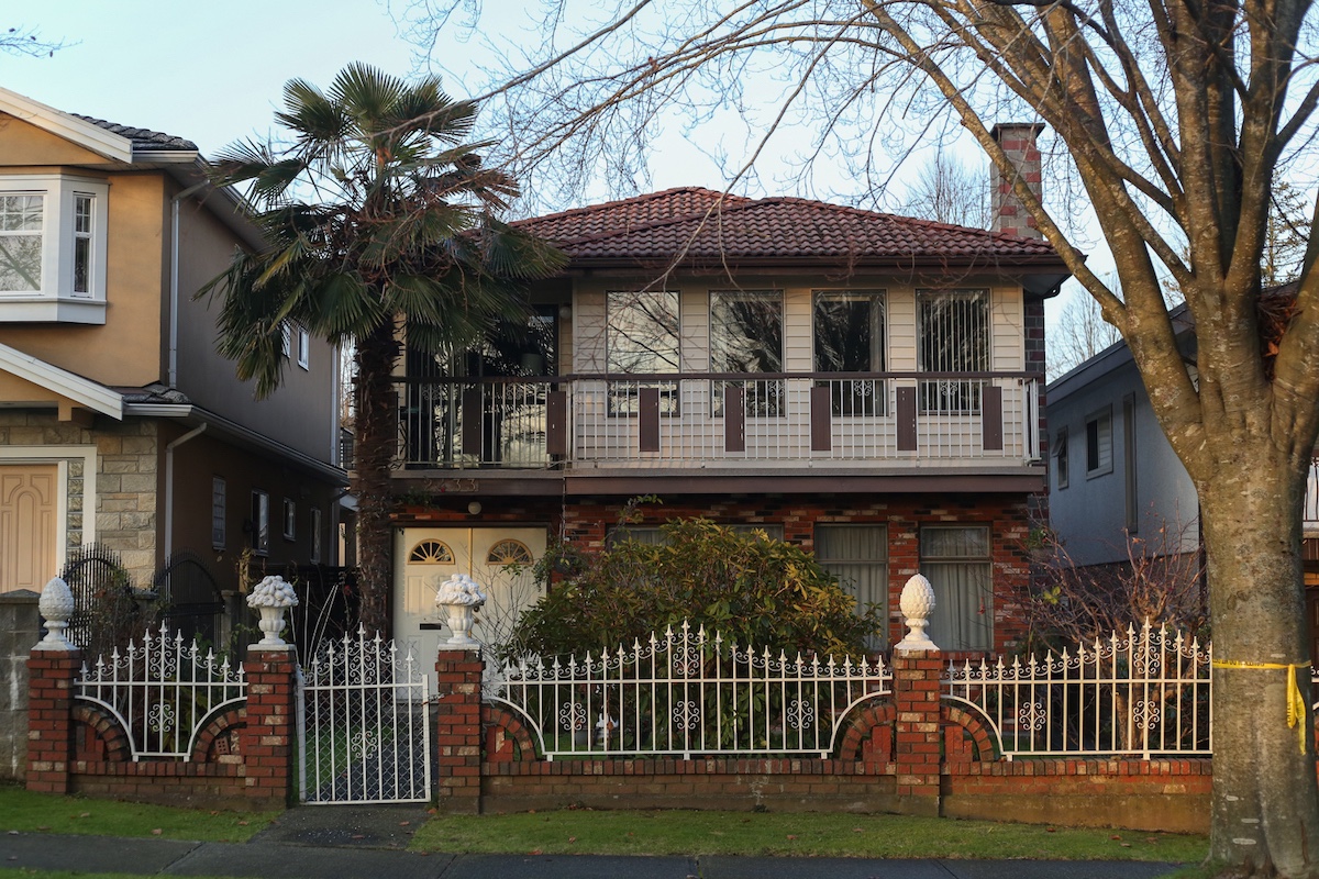 A bricked Vancouver Special with fruit bowls and pineapple ornaments on the gate.