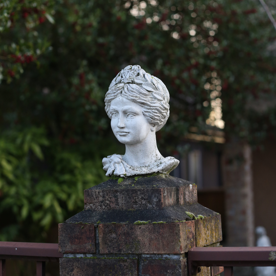 A little concrete figurine of a goddess's head on the post of a brick fence.