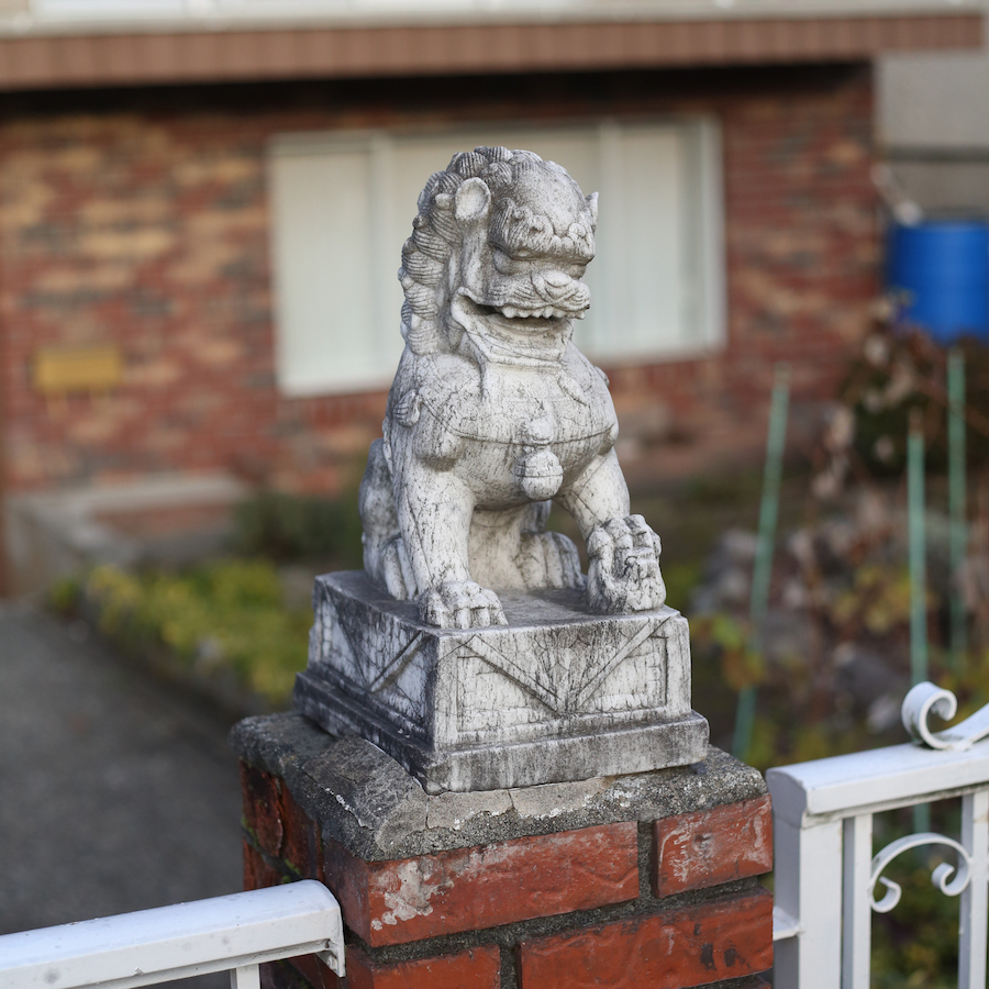 A little concrete figurine of a stylized lion on the post of a brick fence.