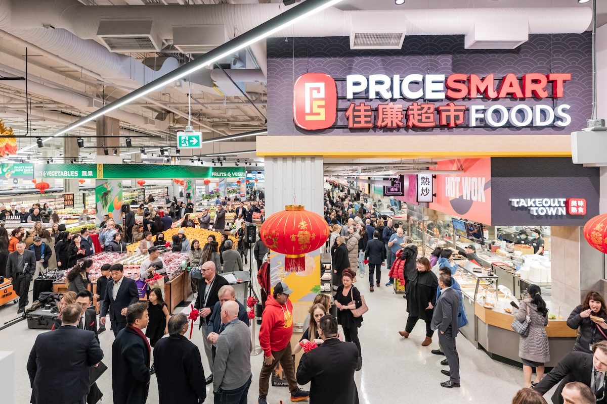 A bustling supermarket with lanterns hanging from the ceiling. The PriceSmart Foods logo in English and Chinese is in bright LED.