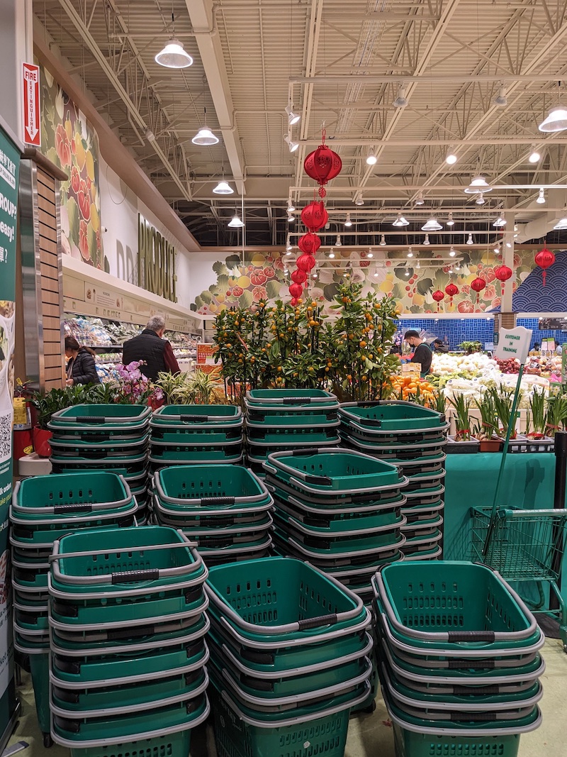 A tower of green shopping carts in front of a pot of orange trees in a supermarket.