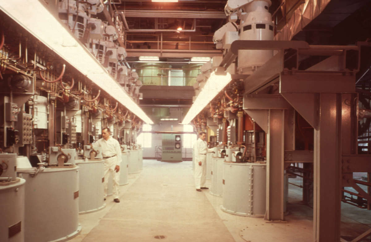 An older photo, from the 1970s, shows a worker in a white shirt and pants attending to machinery.