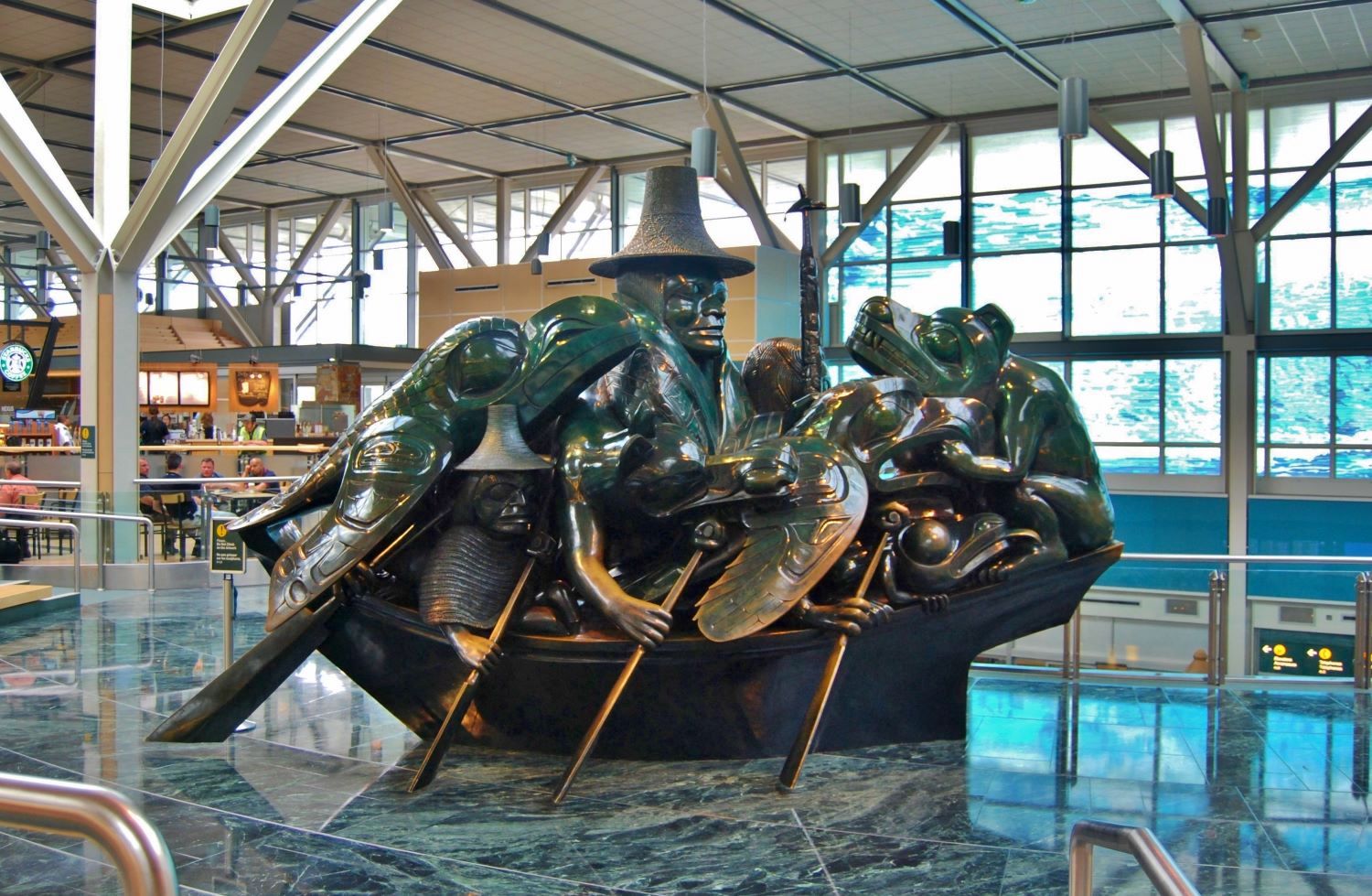 A large bronze sculpture of a Haida person surrounded by animals in a canoe is prominently displayed in an airport.