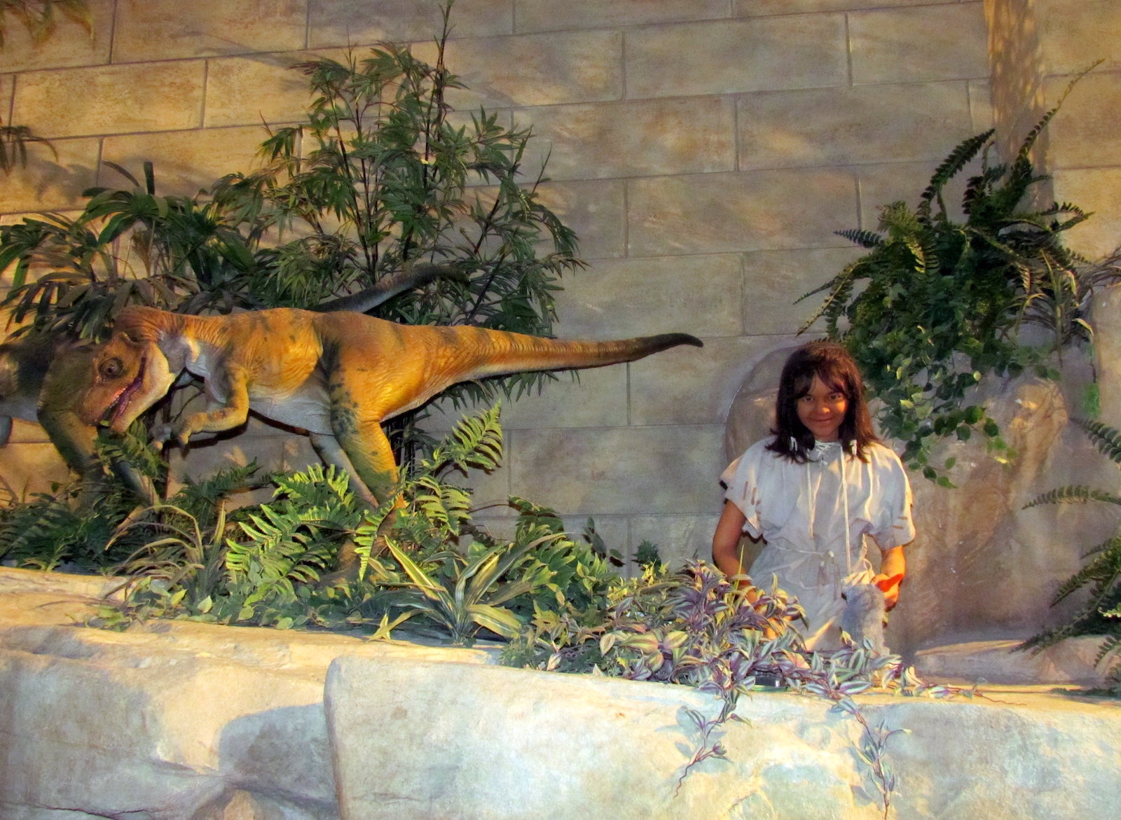 A somewhat creepy-feeling exhibit of a young girl near a velociraptor. They are surrounded by plastic ferns and other foliage.