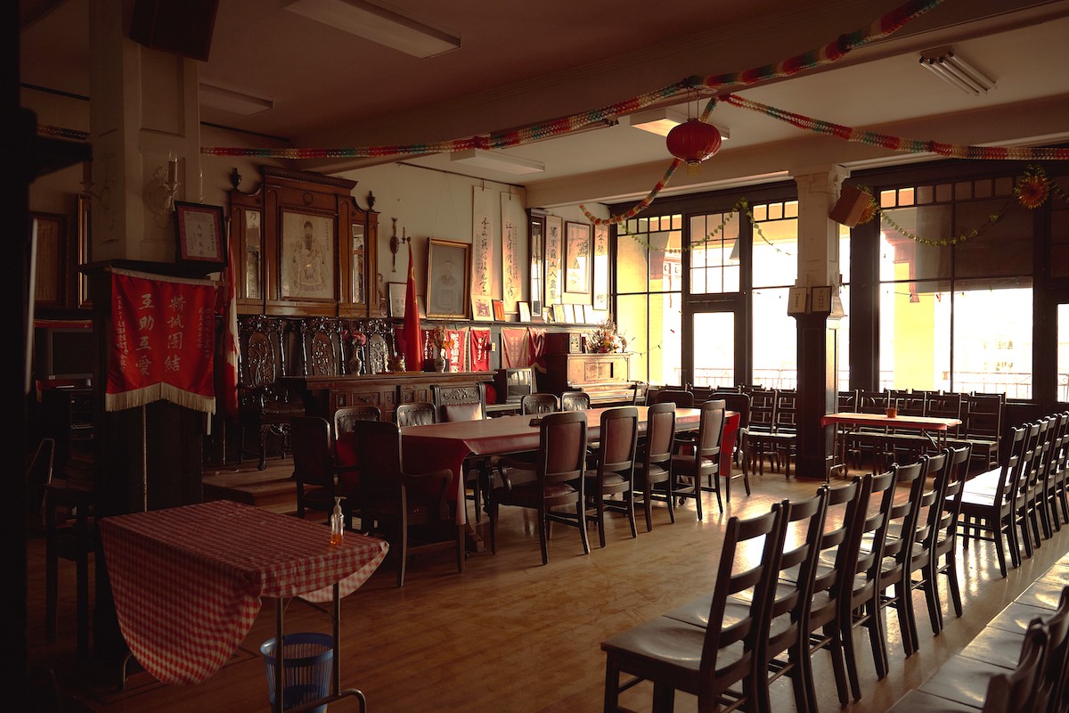 An indoor gathering space features neat rows of wooden chairs and an ancestral Chinese altar at the front of the room.