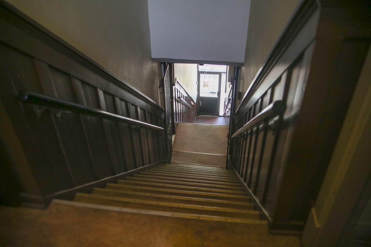 The view down an old narrow wooden staircase with dark wood panelling on either side.
