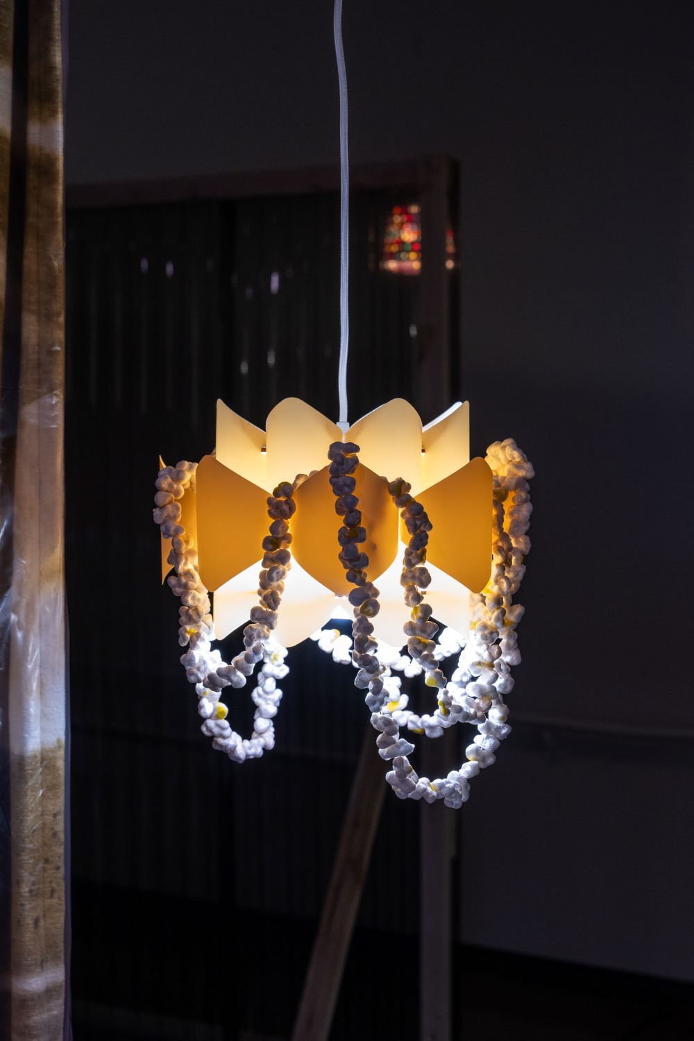 A ceiling lamp made of beige and yellow plastic glows in the dark, with what appears to be popcorn strings draped on it.