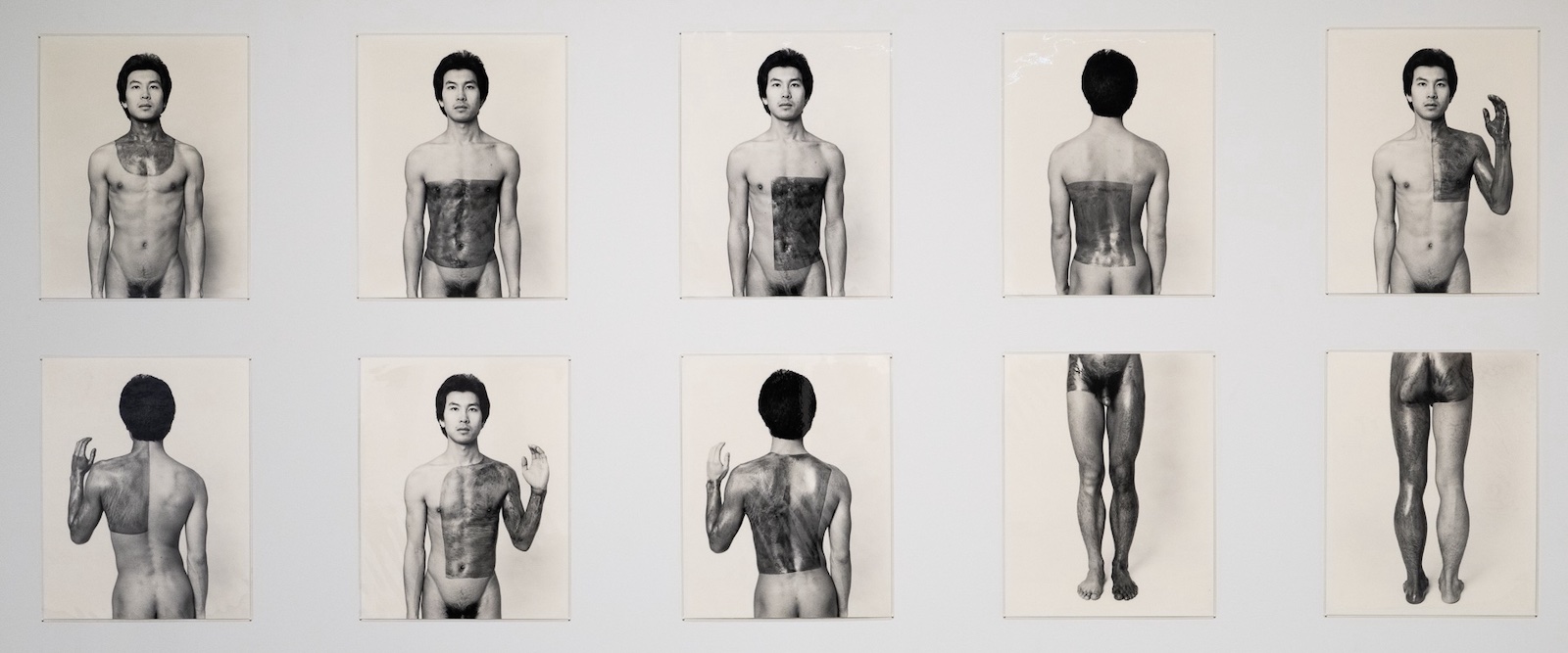 Two rows of vertical black and white prints depict Theodore Sasketche Wan, nude and painting different areas of his body with a dark antiseptic material. The photos depict him facing towards and away from the camera.