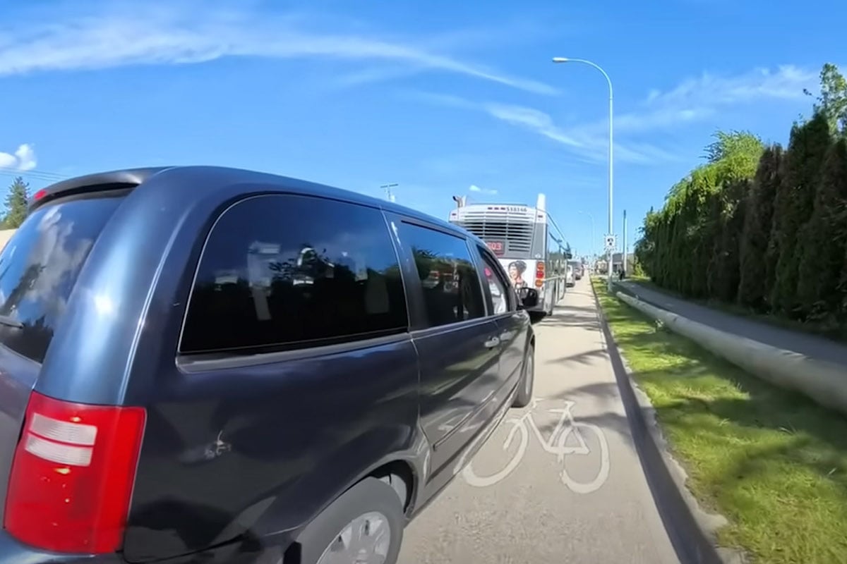 A line of minivans, buses and other vehicles take up space in a painted cycling lane.