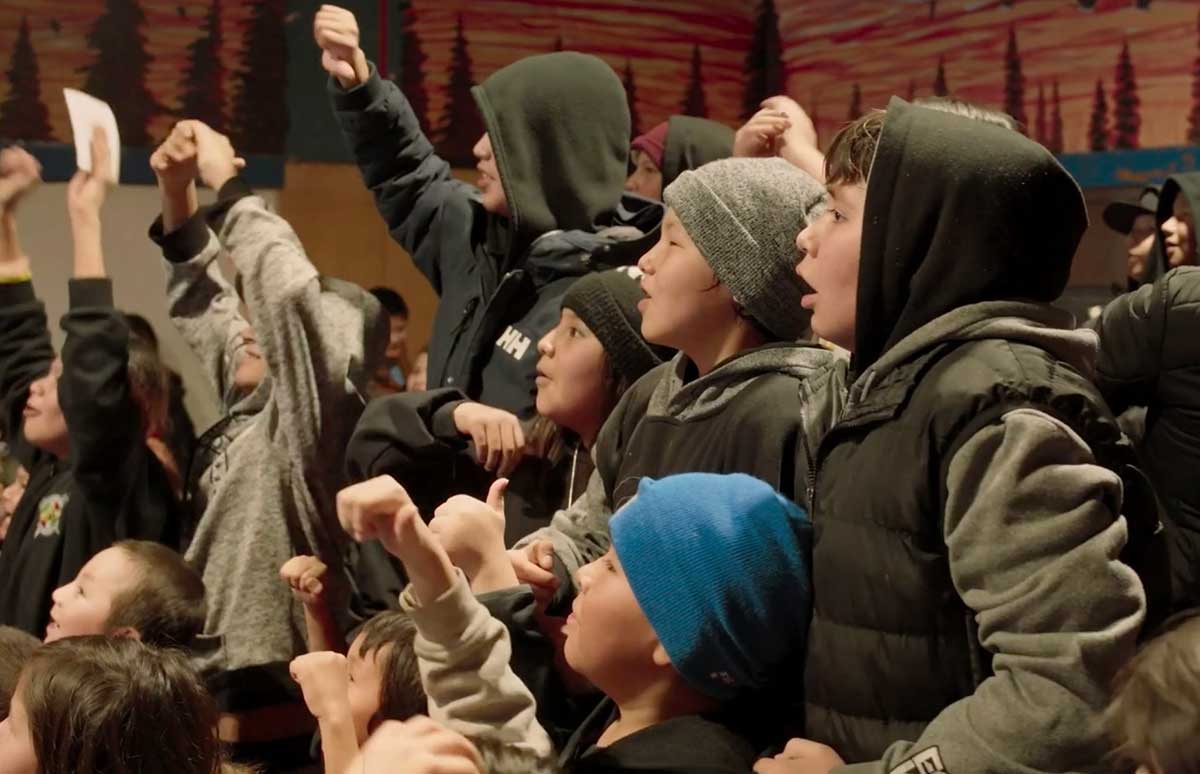 Indigenous elementary school children in an audience feature excited, joyful faces.