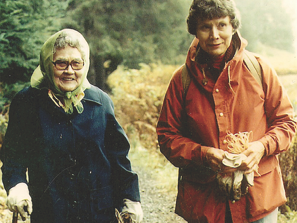 An older photo shows two women outdoors, both wearing gloves. Delores Churchill, on the right, is holding some fibre. Her mother is using a cane.