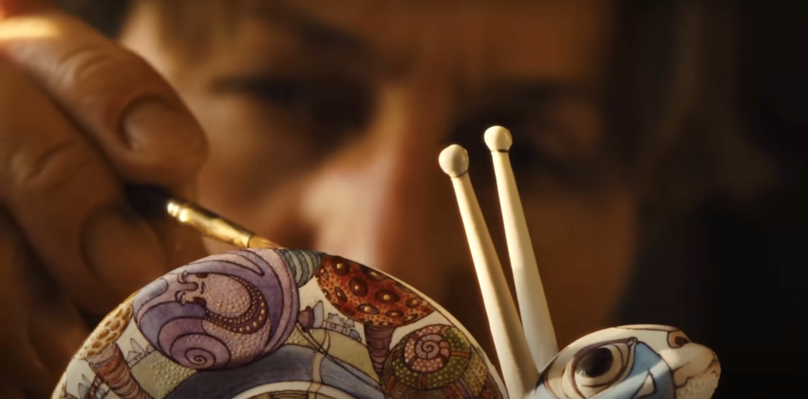 A hand paints a delicate porcelain snail whose body contains fantastical, cartoonish images in many colours.