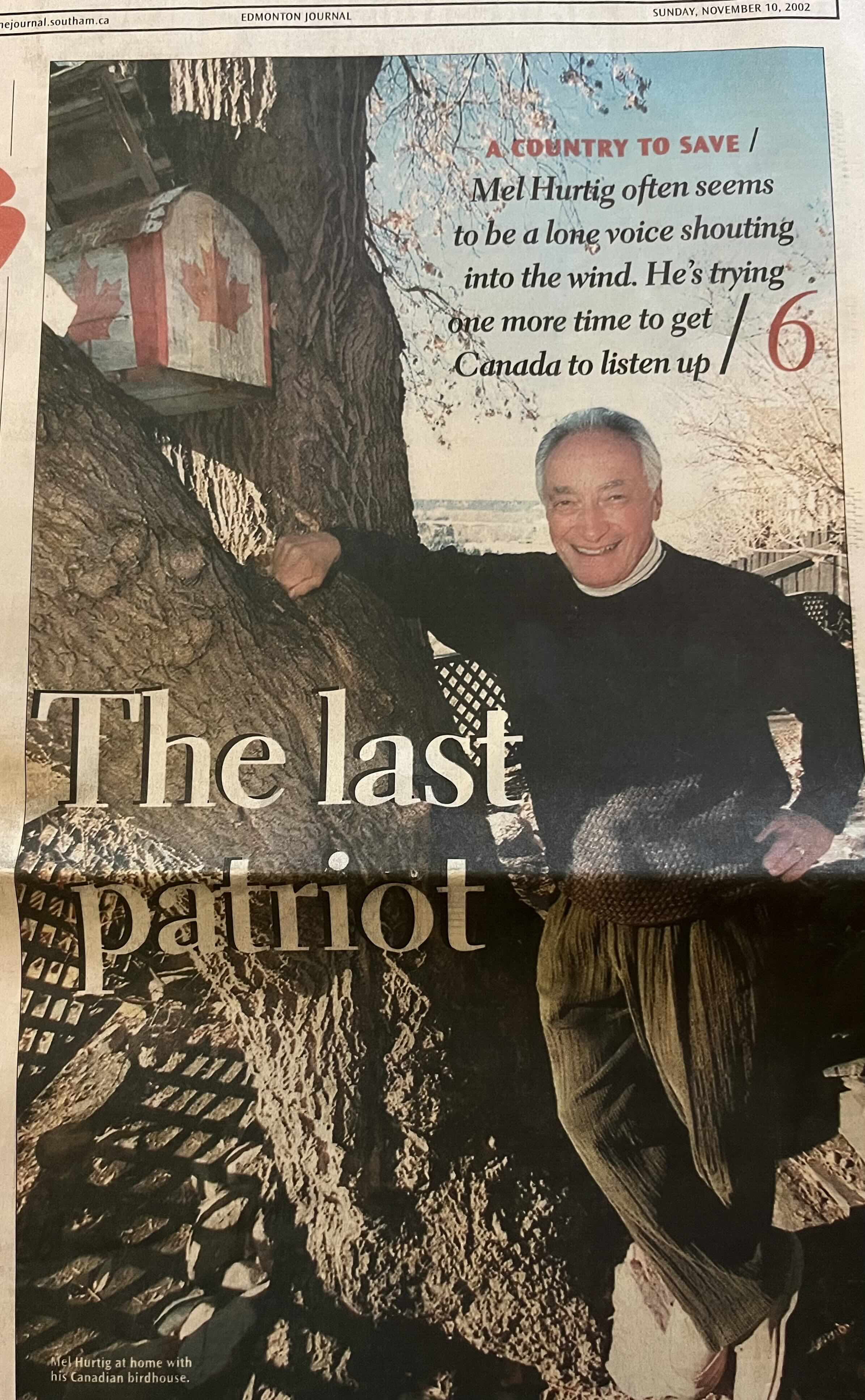 A colour photograph of a clipping from a broadsheet newspaper features Mel Hurtig, a man with grey hair, a dark sweater and olive-coloured corduroy trousers, standing next to a tree and leaning with one arm on its trunk. He is smiling at the camera and the tree holds a birdhouse bearing the Canadian flag. The newspaper headline reads “The last patriot.” Copy above Hurtig’s head reads “A country to save: Mel Hurtig often seems to be a lone voice shouting into the wind. He’s trying one more time to get Canada to listen up.”