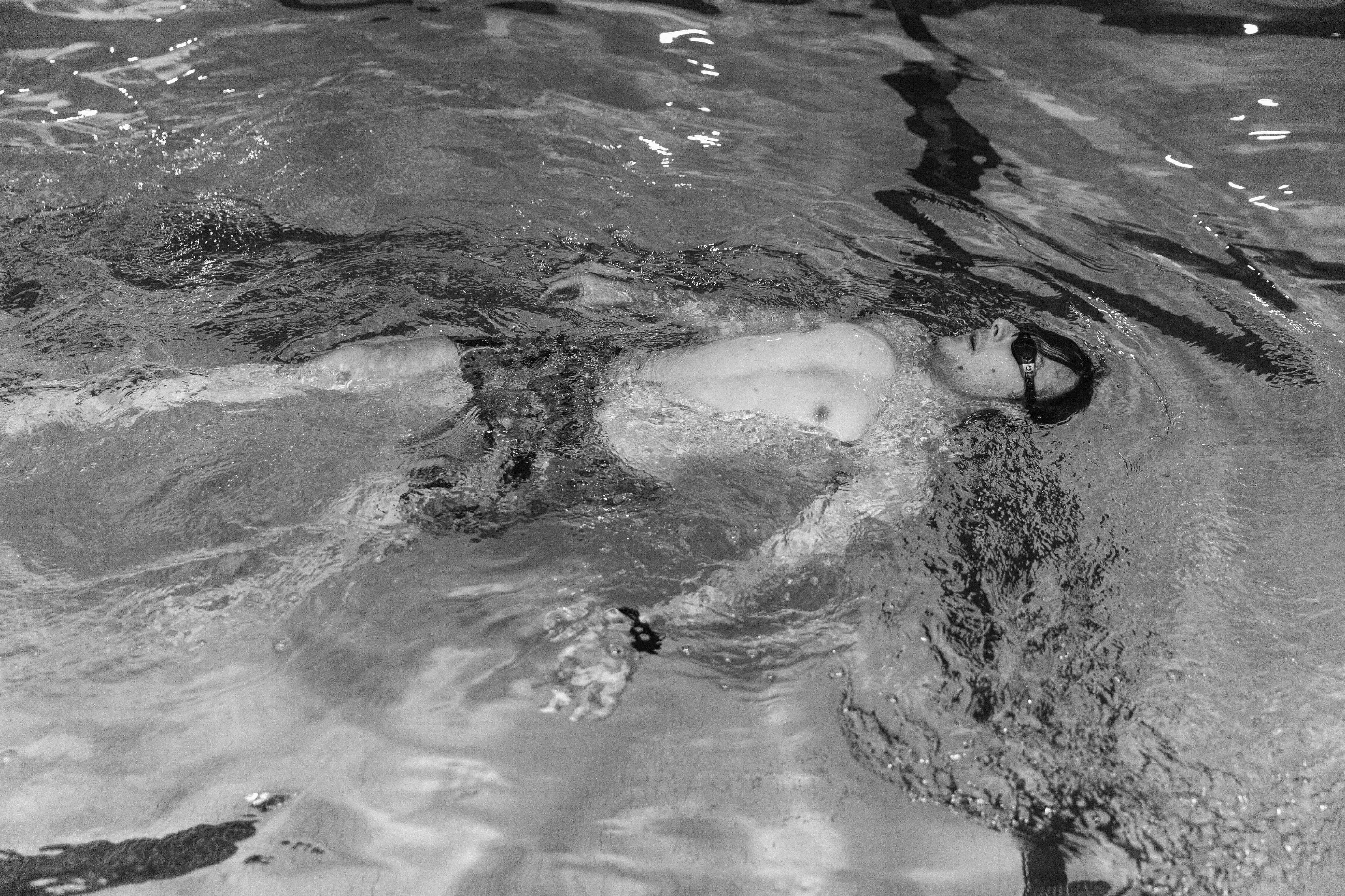 Jeremy Kalicum has short dark hair and is wearing goggles, a watch and swim trunks. He floats on his back in an indoor pool.