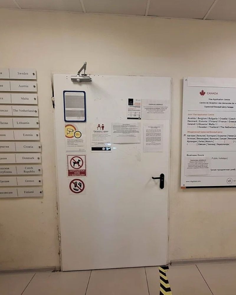An image of a poorly lit room and a white door with numerous signs in a foreign language. On the left side of the door is a sign with the Canadian maple leaf insignia.
