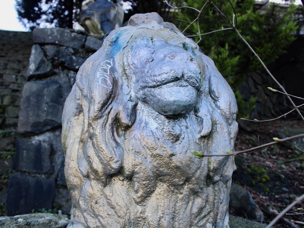A statue of a lion. The top half of the lion has been painted a light blue. The bottom half has been painted a light gold.