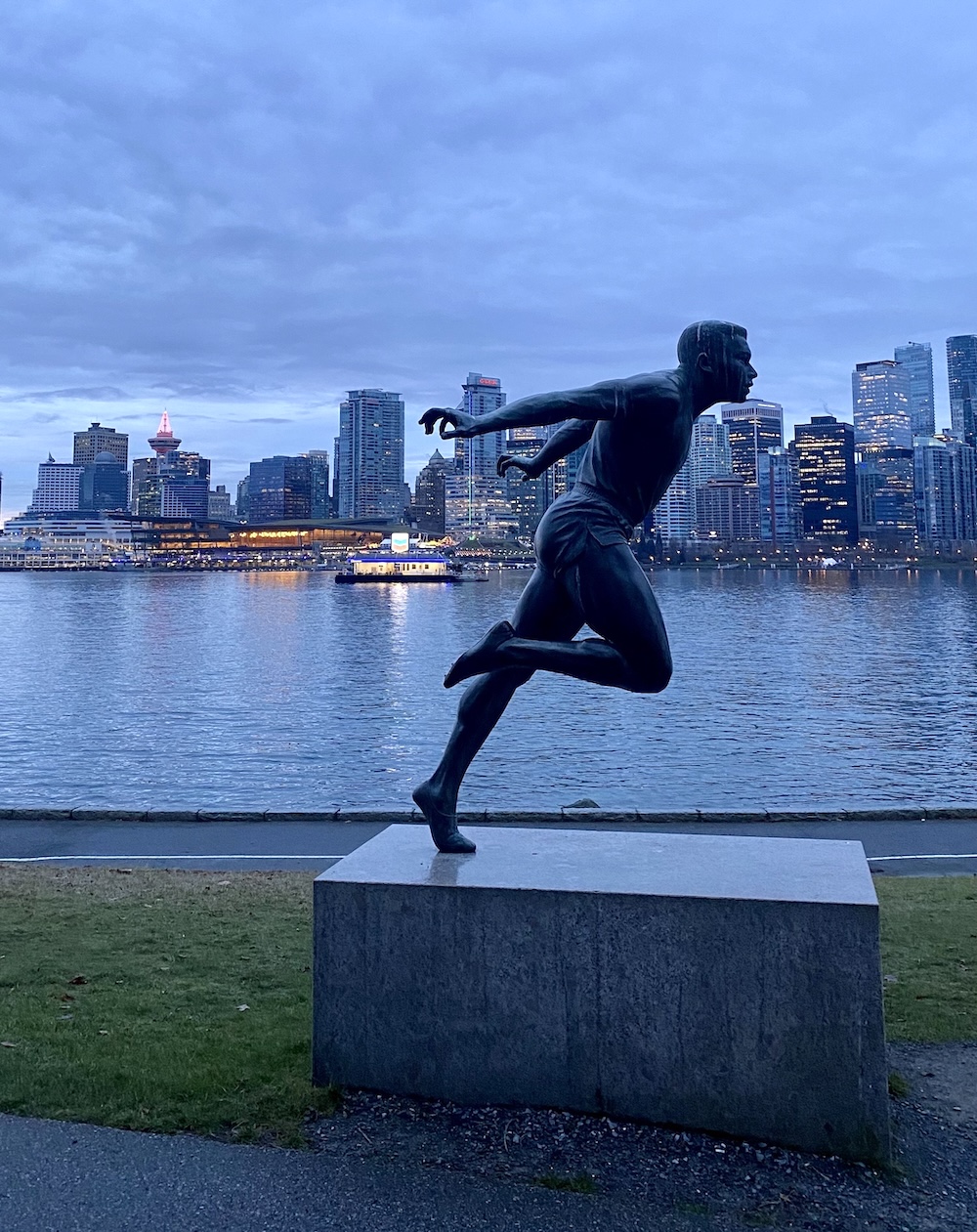 A statue of a runner, with the harbour and the Vancouver skyline in the background.