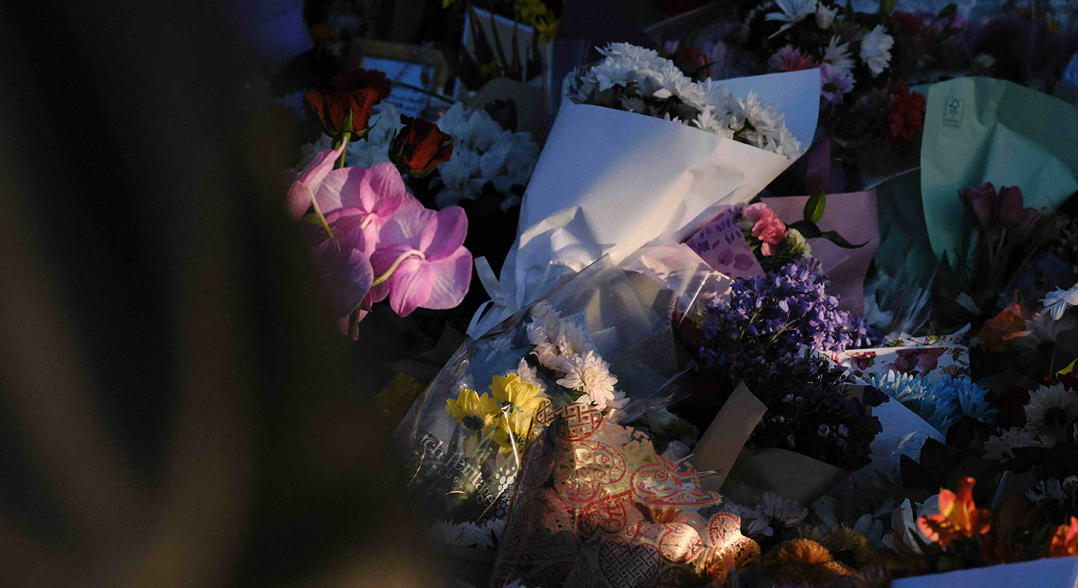 Bouquets of flowers wrapped in paper and plastic are assembled on top of each other in fading sunlight.