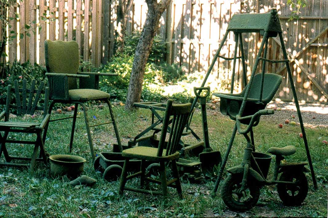 Furniture and toys are coated in green powder and arranged in the grass in what appears to be a residential backyard.