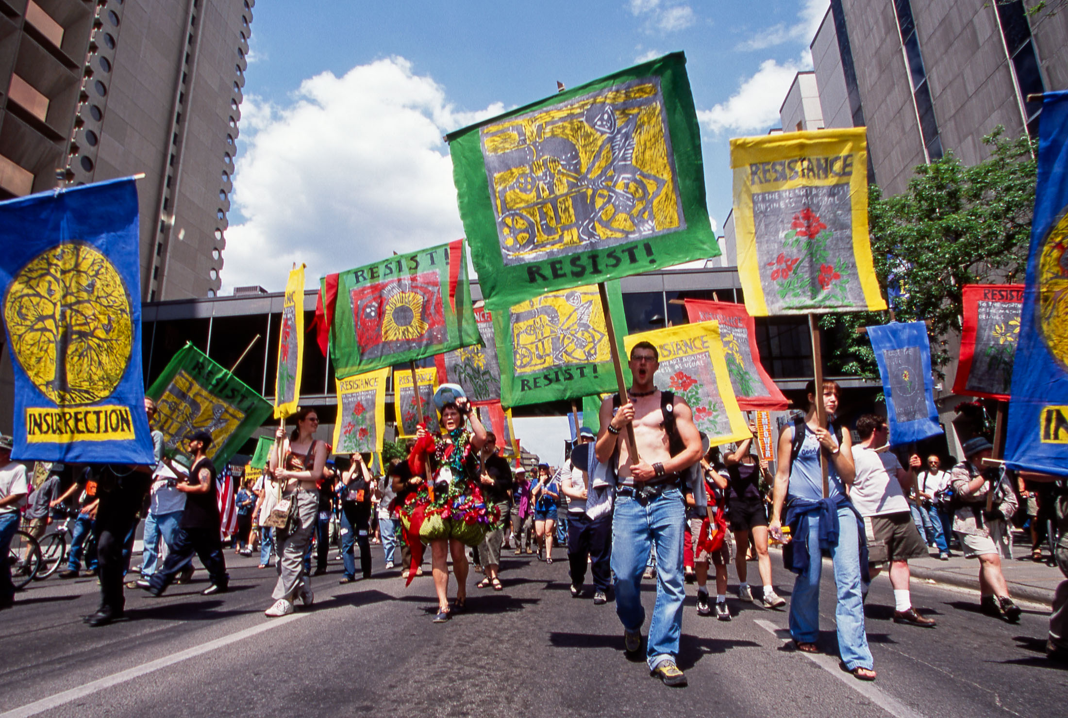 Protesters march down a street in downtown Calgary holding large illustrated signs in green, yellow, blue and red. 