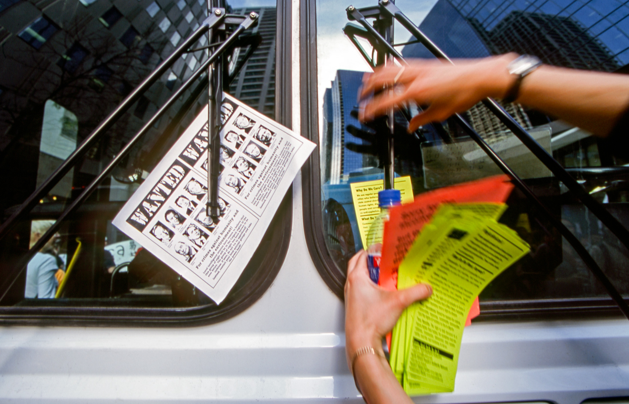 A pair of hands places colourful pamphlets under the windshield wipers of a white van.