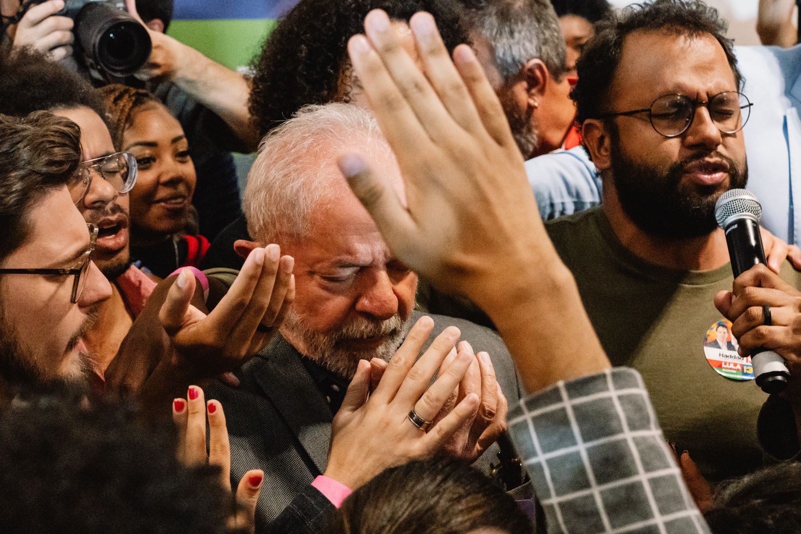 A late middle-aged grey haired man prays surrounded by a cluster of other praying people.
