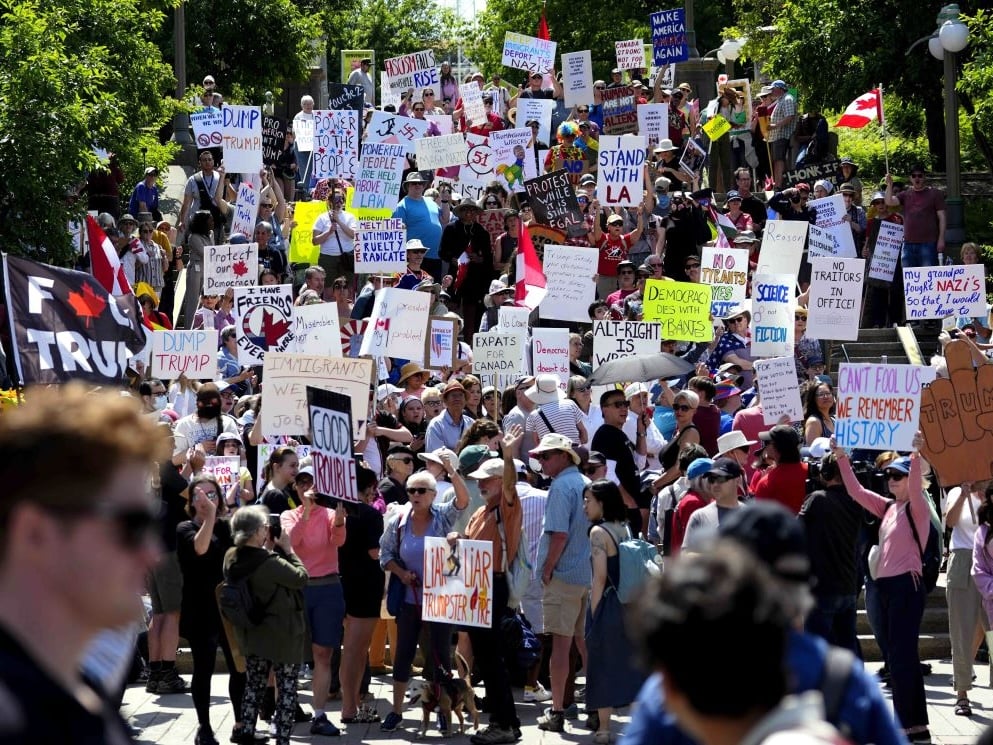 Protesters fill an outdoor space holding many signs, including ‘Liar Liar Trumpster Fire,’ ‘Dump Trump’ and ‘Good Trouble.’