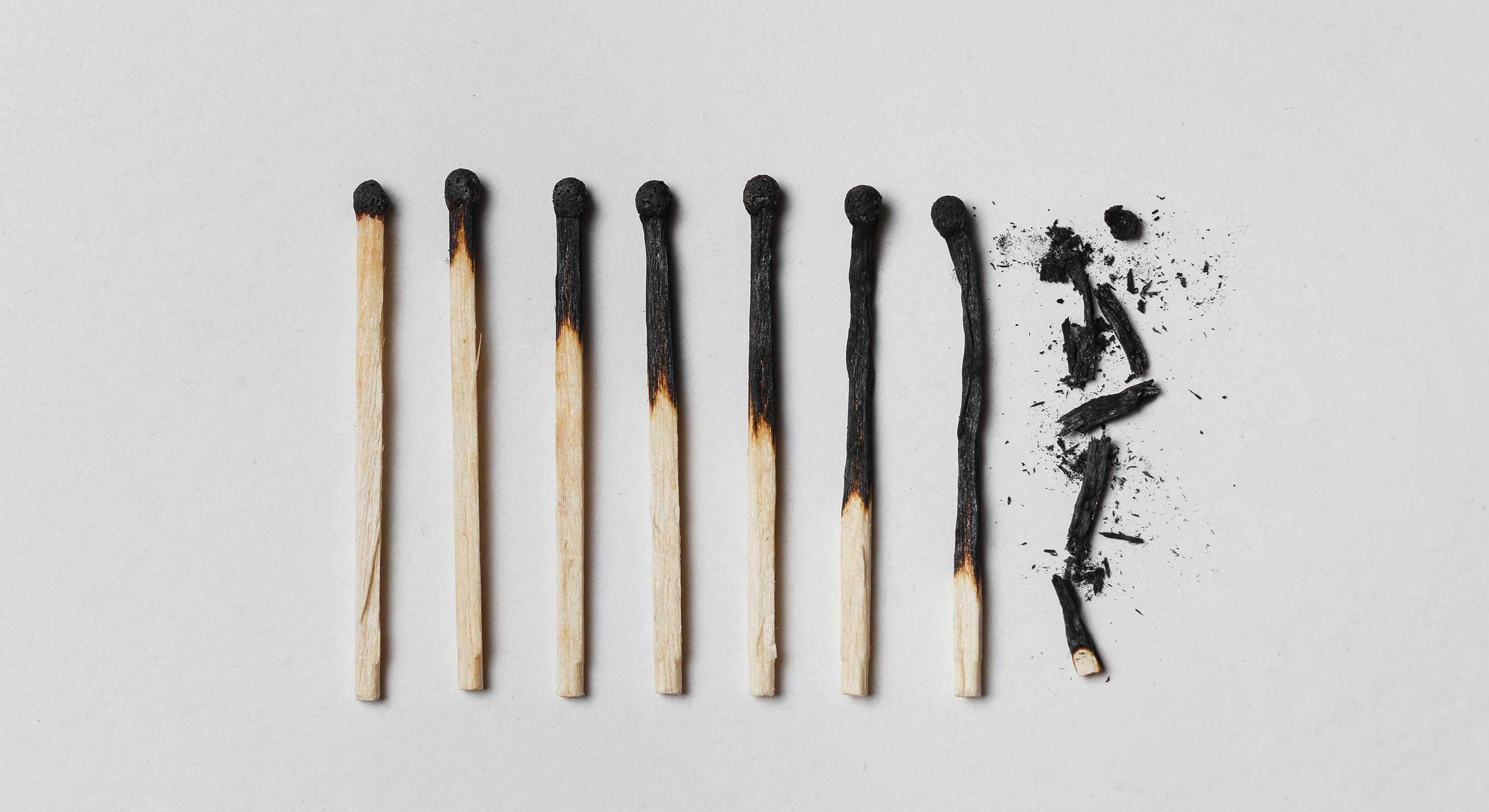 Eight burnt matches are arranged across a flat white surface. From left to right, they are least- to most-burnt.