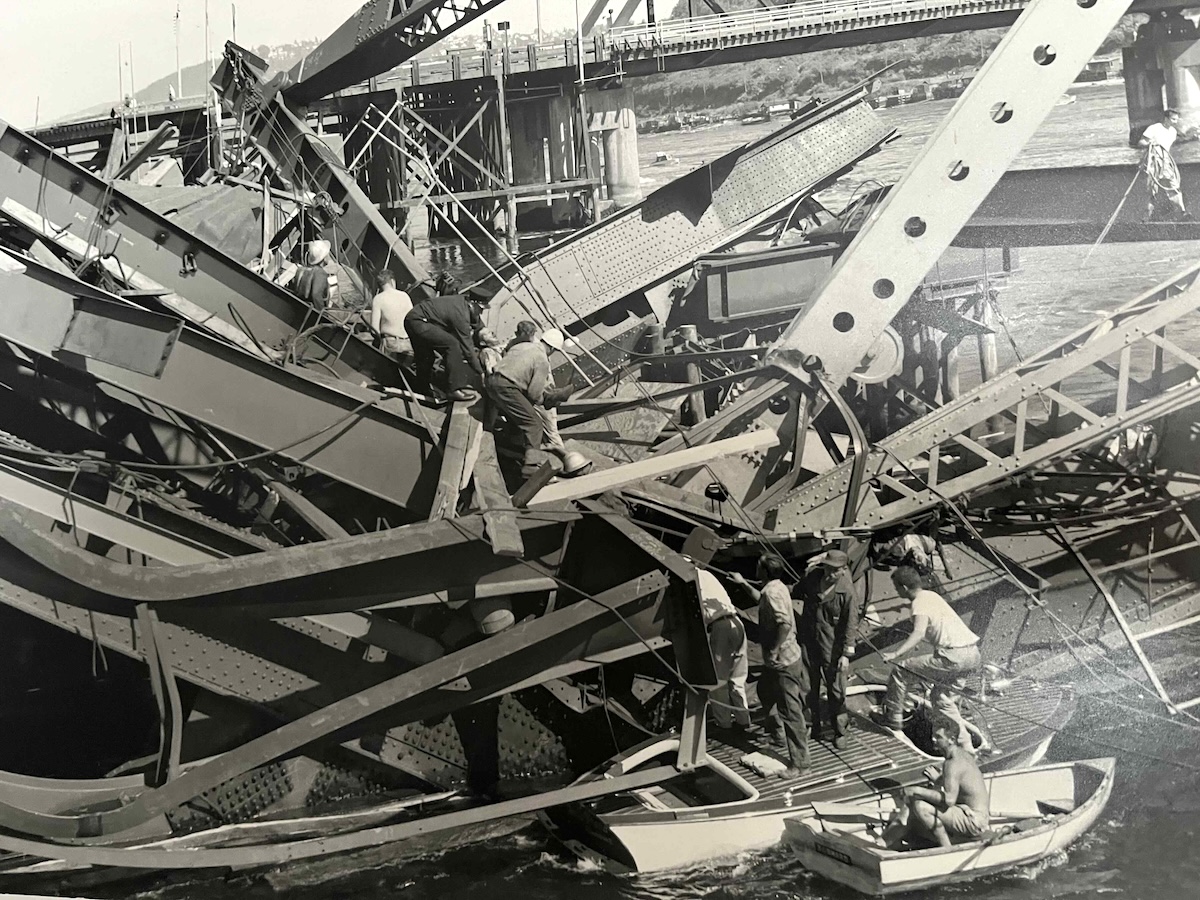 A shirtless man is in a small rowboat as rescuers scramble over the wreckage of the Ironworkers bridge.