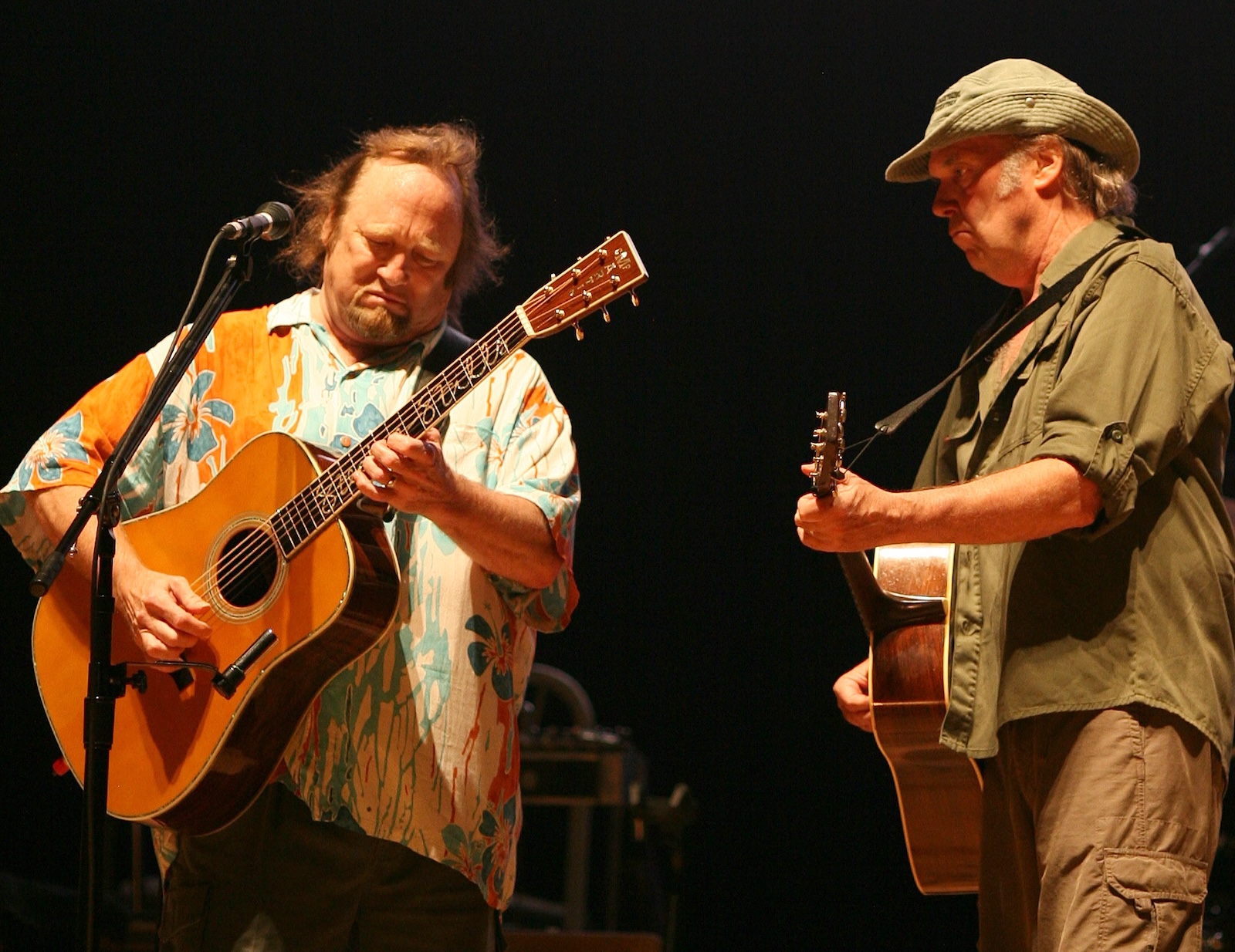 Two white men in late middle age play guitars on stage.
