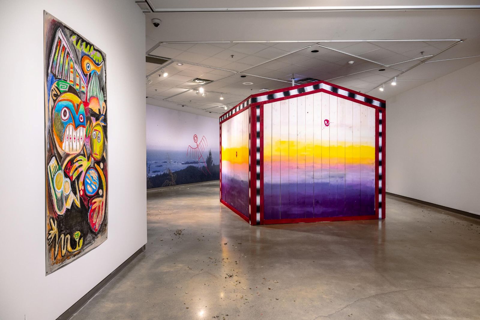 Top: a close-up photograph depicts the detail from the prismatic side of a longhouse wall in lavender, yellow and pink. A fuschia graffiti-like drawing is scrawled across it. Bottom: the installation view of an art gallery featuring a large-scale installation of a First Nations longhouse in prismatic white, yellow, orange, lavender and indigo. To the left on the wall is an abstract painting featuring animals drawn in psychedelic rainbow colours.