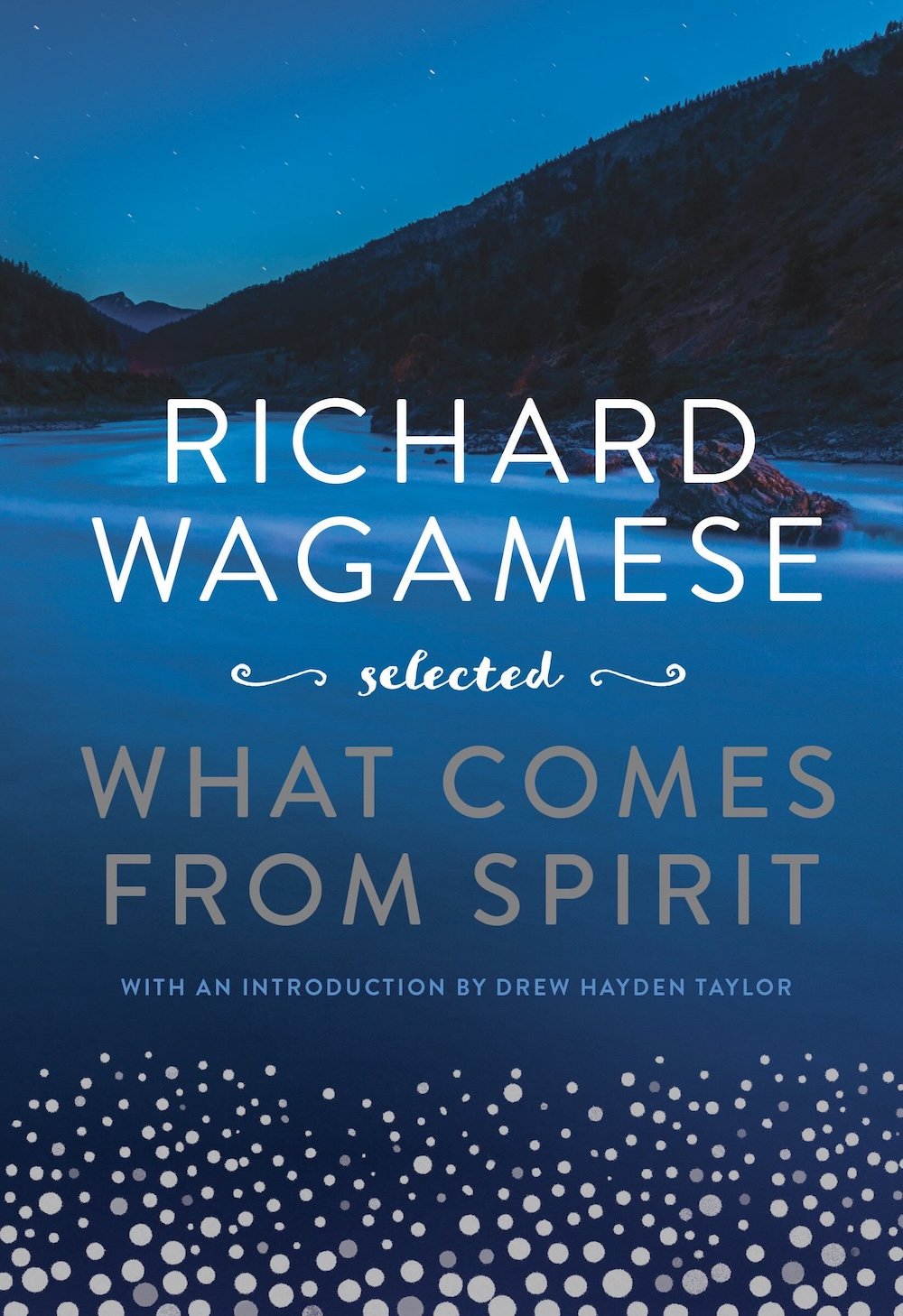 The book cover image for ‘Richard Wagamese Selected: What Comes from Spirit’ features white and silver title text against a blue background featuring water against dark mountains and a blue sky. Digital silver dots are assembled at the bottom of the frame.