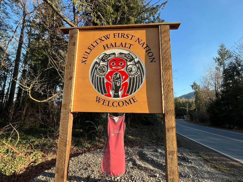 A wooden sign with a Coast Salish crest welcomes visitors to Halalt First Nation.