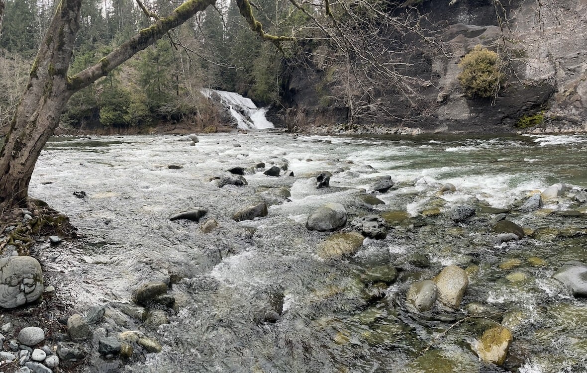 In the foreground, water descends over a series of rocks. In the distance, a large cascade is visible. 