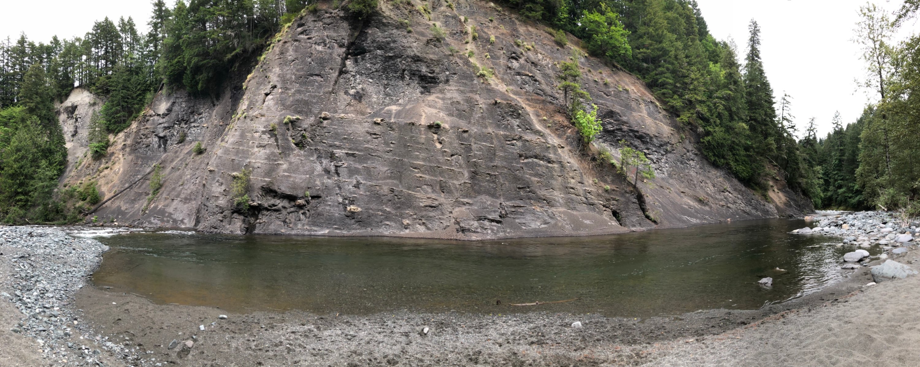 A wide-angle photograph shows a slow-moving river passing a sheer cliff. The river picks up pace on either side of the cliff.