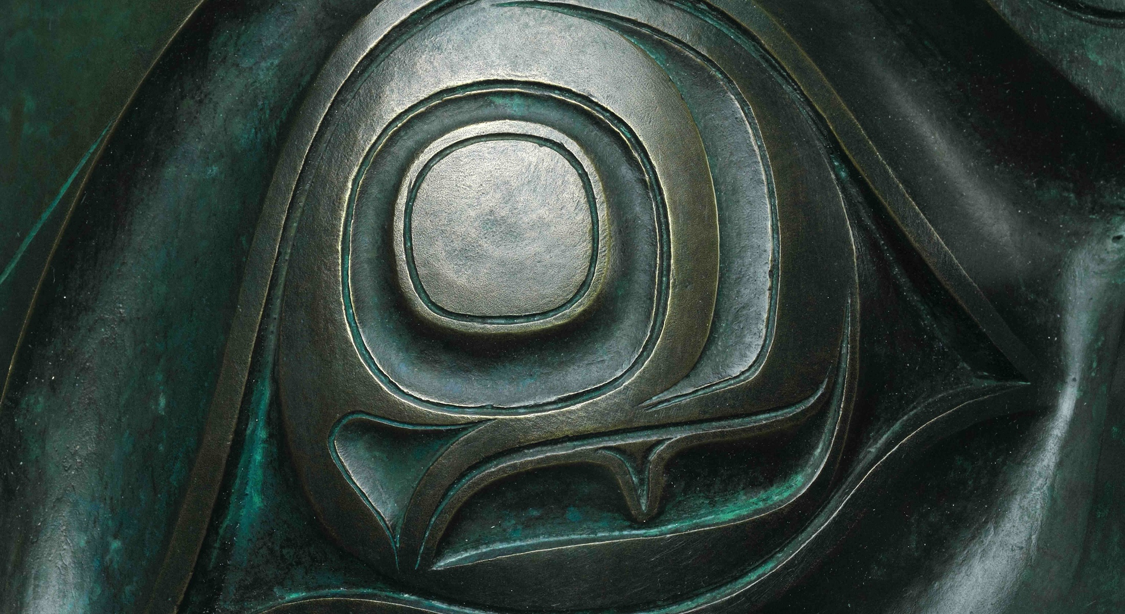 The detail of a bronze eye with green markings from a large piece of Haida artwork.