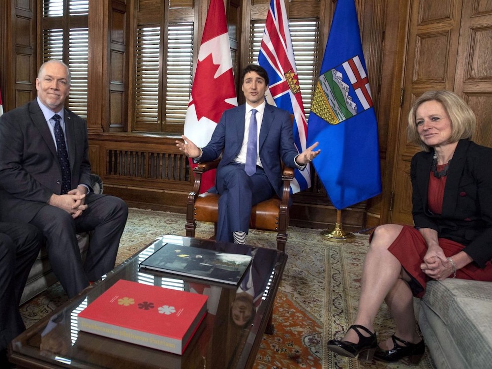 Three people sit in a wood-panelled room in front of flags.