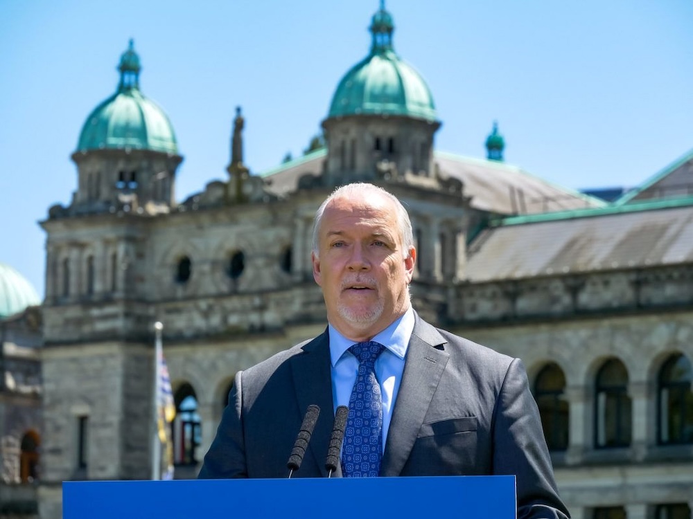 John Horgan, a middle-aged light-skinned man with trimmed grey hair and goatee, stands outside the Legislature.