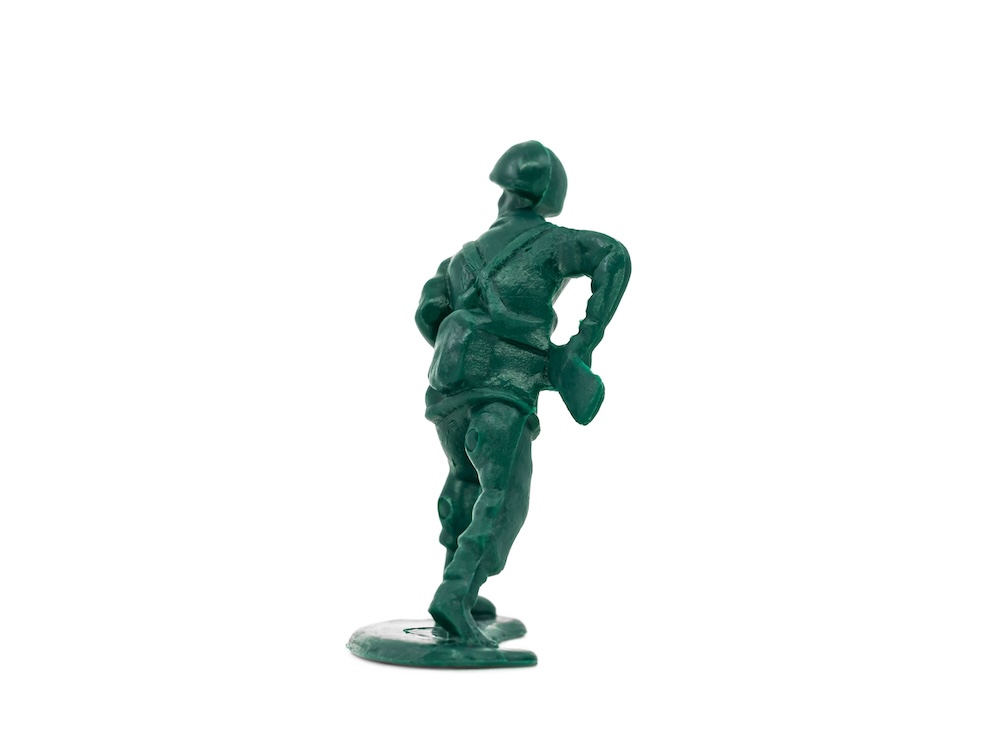 A green toy soldier stands against a white background with its back to the camera.