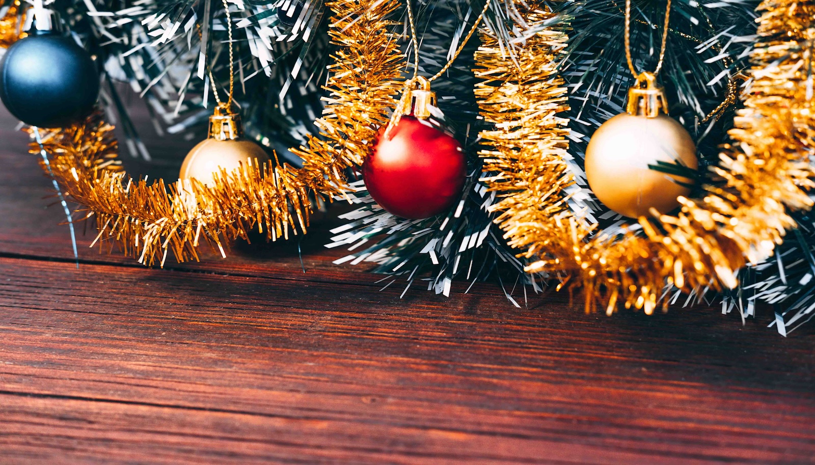 Round colourful Christmas ornaments adorn the lower branches of a Christmas tree against wood flooring.