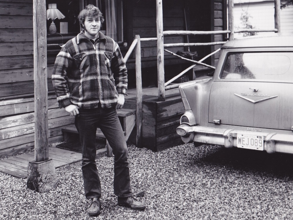 A large 17-year-old teenager is shown in a black and white photo from 1975. He has large sideburns and is wearing a zip-up plaid sweater.