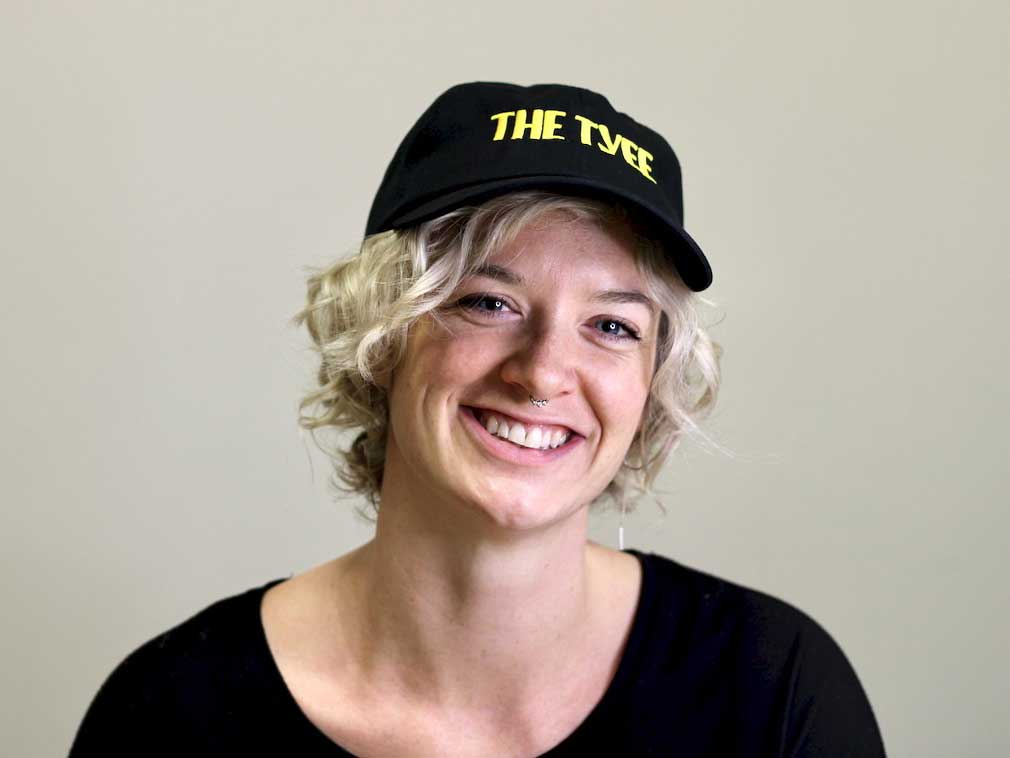 Michelle Gamage has short curly blond hair and a light skin tone. She is wearing a black ball cap with the words &ldquo;The Tyee&rdquo; in all caps yellow text. She is wearing a black top.