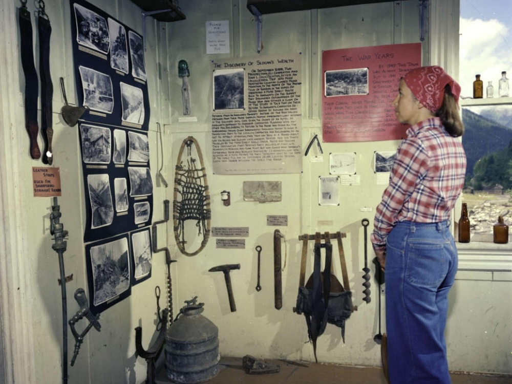 A woman wearing a checkered shirt and jeans clasps her hands while looking at a series of historic photos.