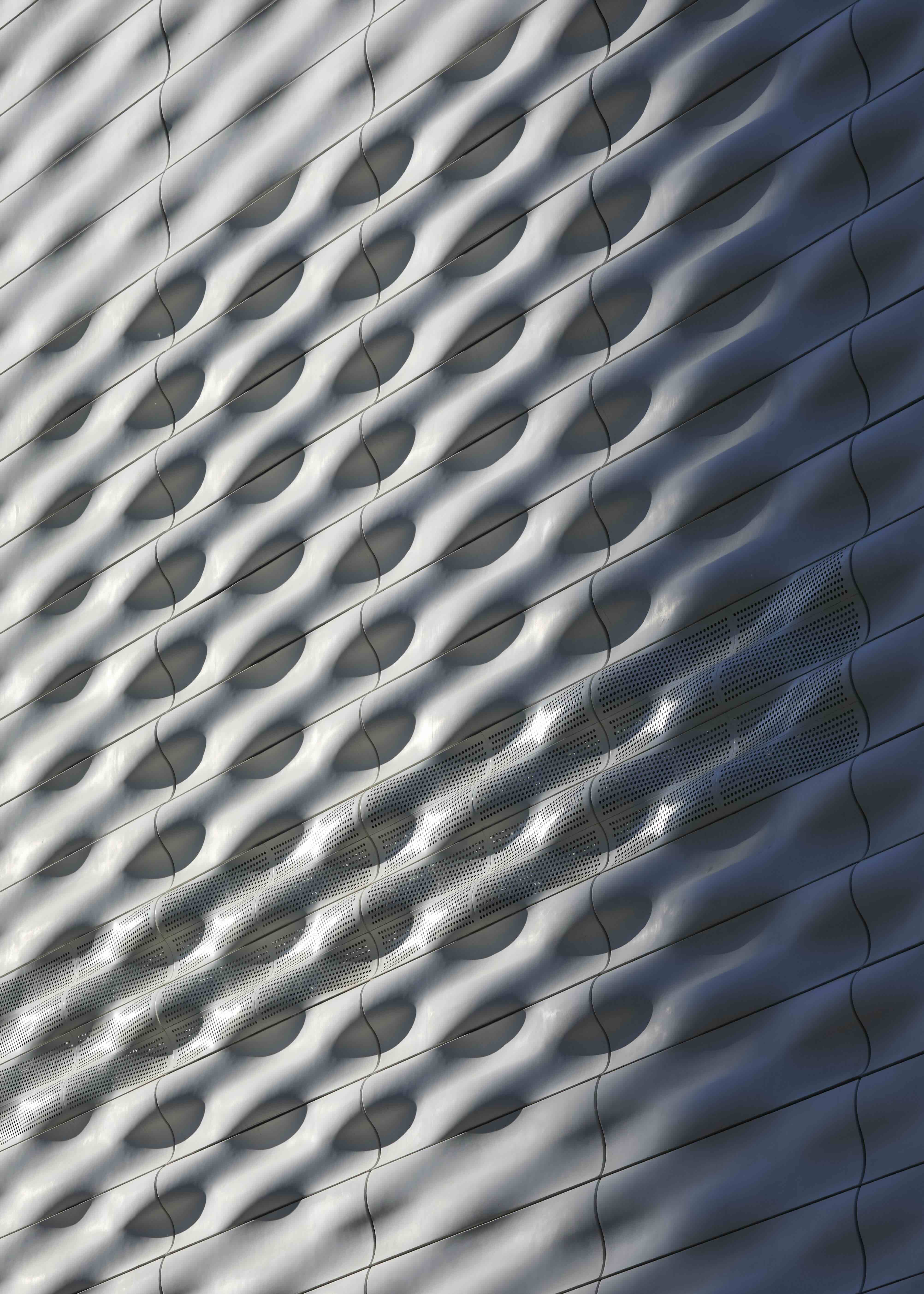 A close-up shot of a white rippled exterior surface of a building shows undulating layers and a shadow to the right.