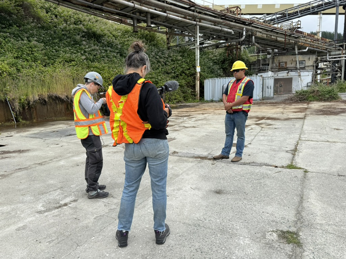 Two videographers hold cameras pointed at Tiy&rsquo;ap thote &ndash; Erik Blaney, who is wearing a safety vest and hard hat. 