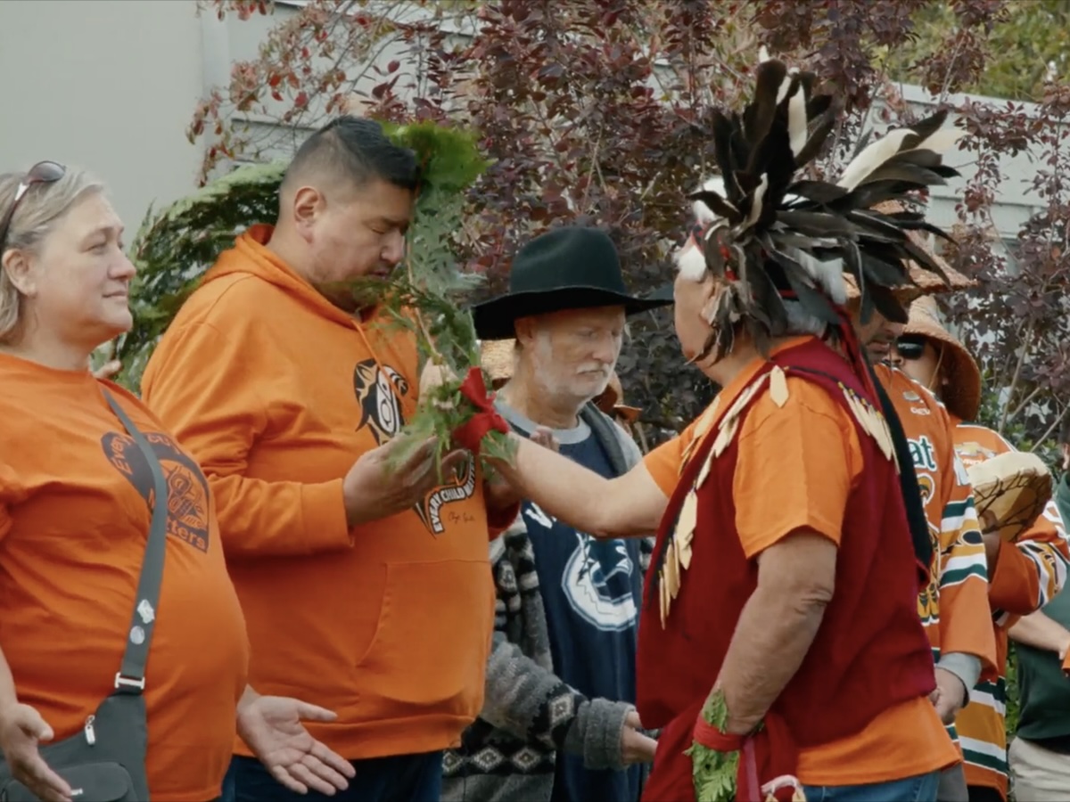 About six people wearing orange shirts, some Powell River city councillors and some Tla&rsquo;amin Nation legislators, are lined up in front of city hall as a Tla&rsquo;amin Elder brushes them with cedar.