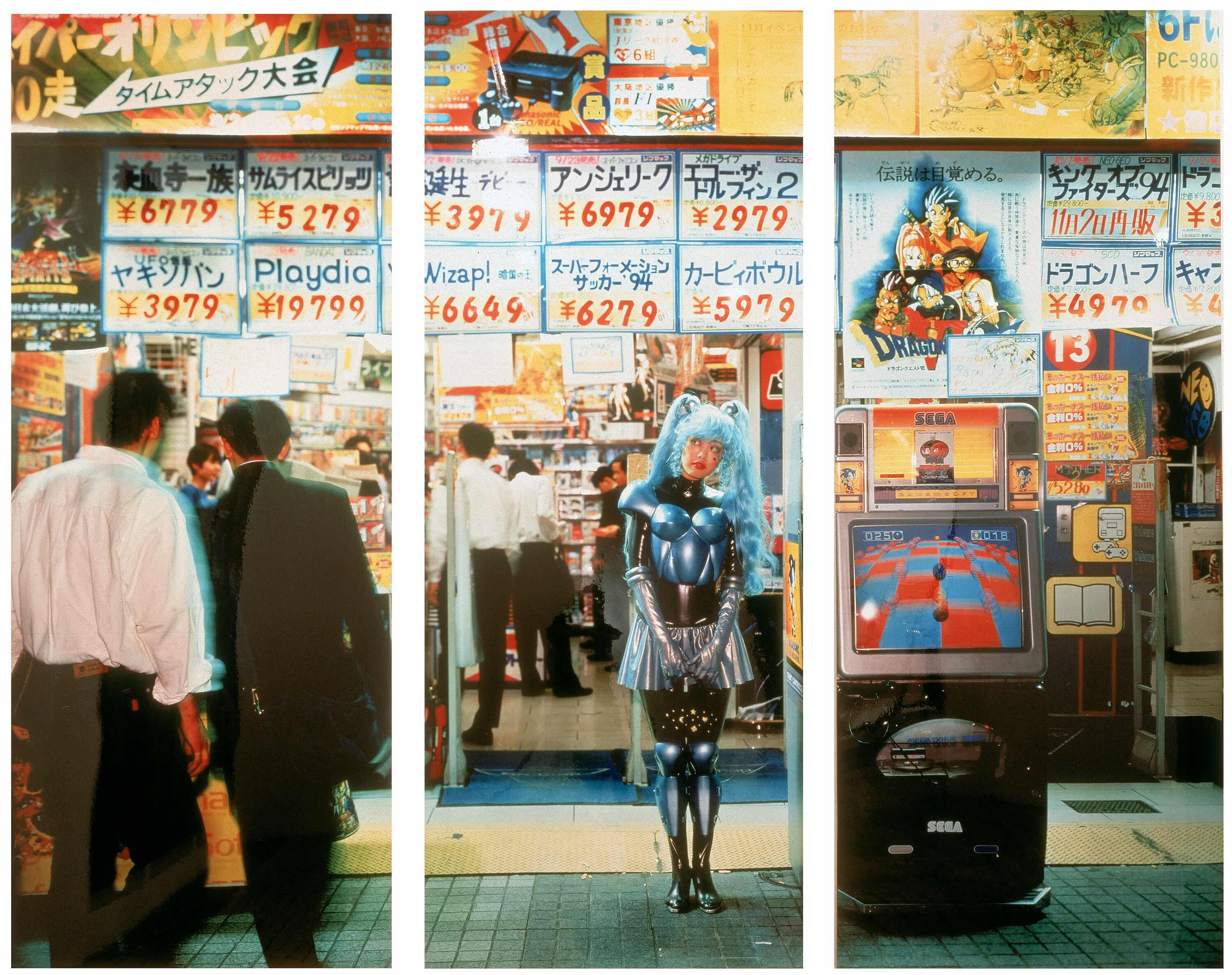 A piece of artwork is divided with white vertical lines across three panels. The photographic work depicts a woman with long light blue hair dressed as a robot. She stands outside an electronics store, looking at two men to the left of the frame whose backs are turned to the camera. The signs in the store are in Japanese.