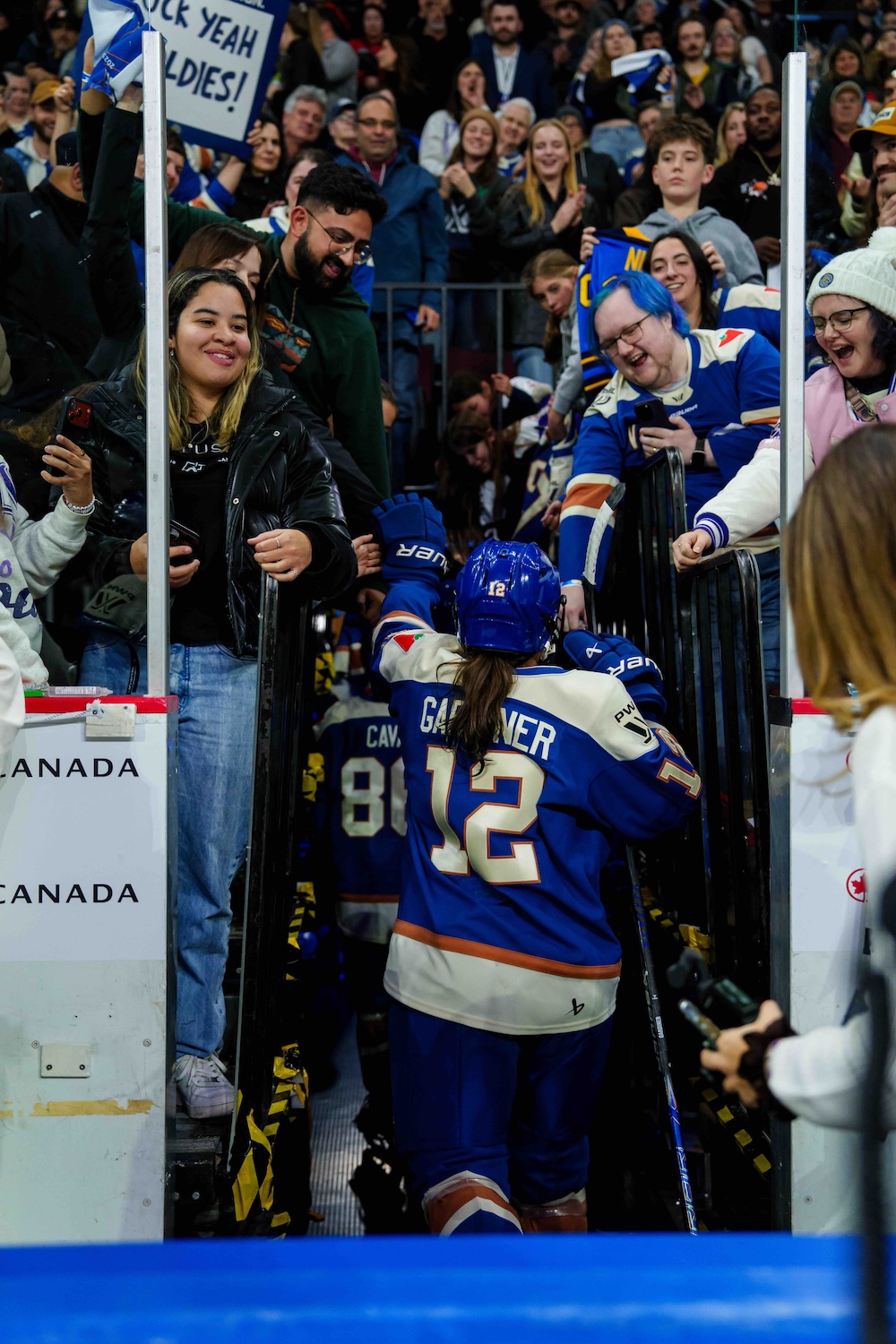 Fans at a hockey stadium, many of them women, reach down to high-five female hockey players as they walk back to their dressing room.