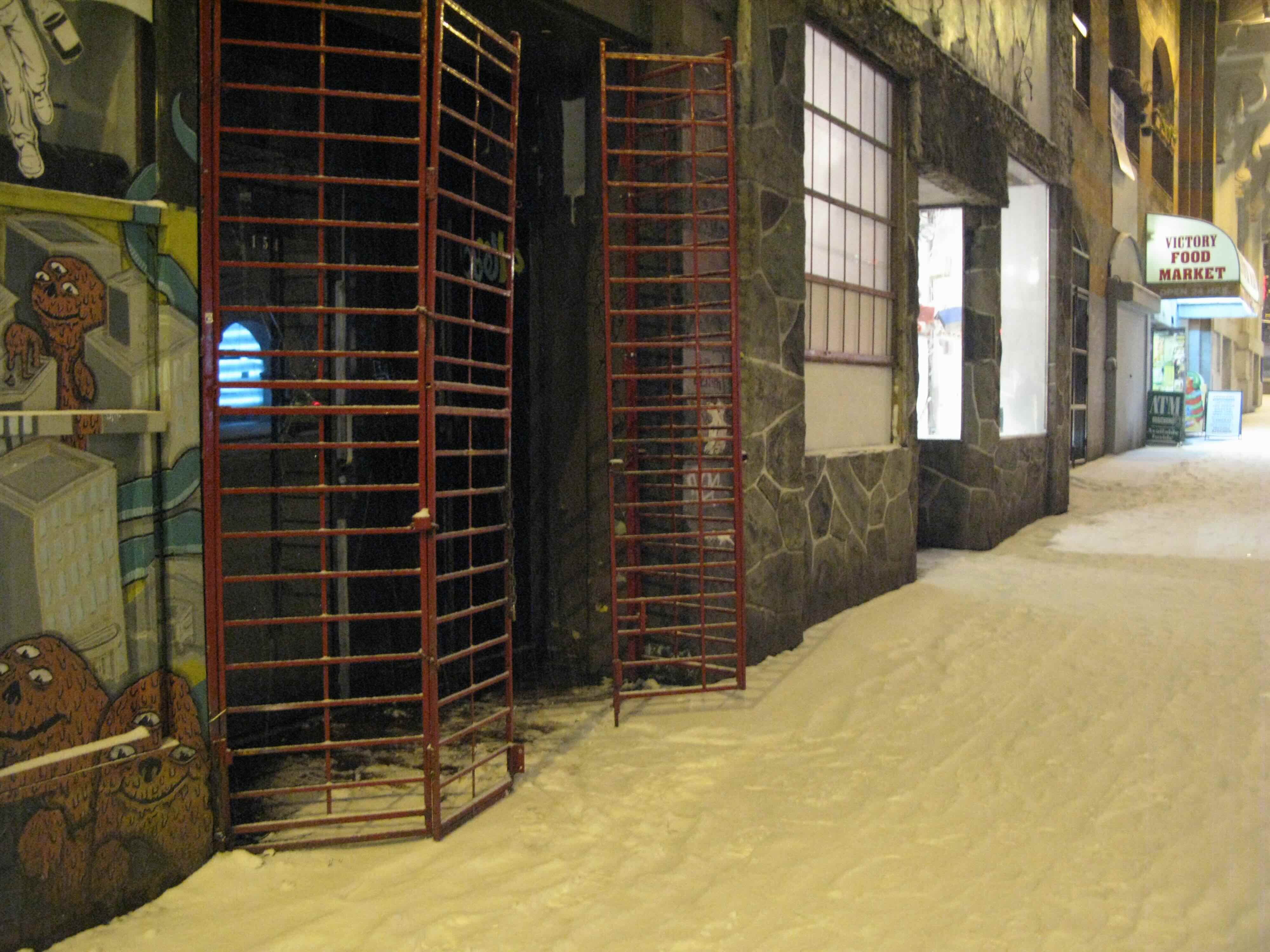 A pair of red gates stand to the left of the frame before a snowy sidewalk at night.